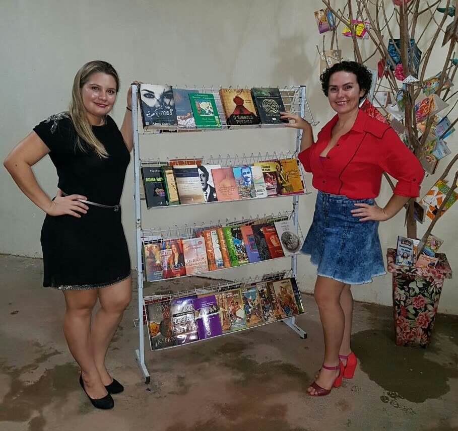 Duas mulheres ao lado de uma estante de livros e de uma árvore decorada com papéis coloridos