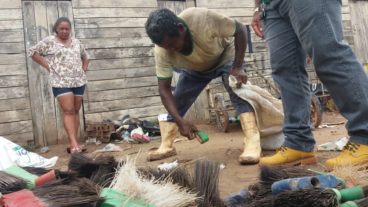 Catador separa vassouras descartadas no chão, observado por integrantes da visita