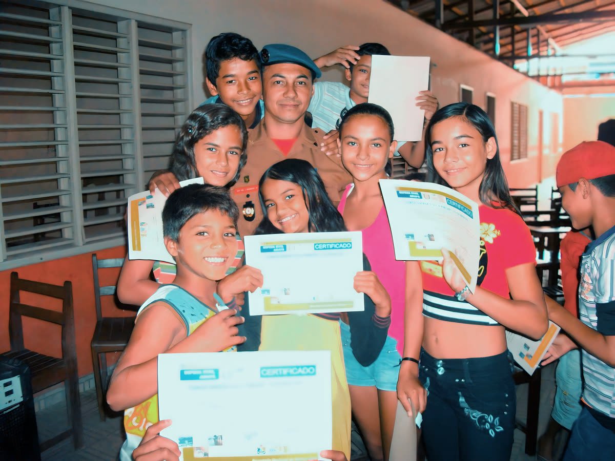 Crianças exibem seus certificados ao lado de um agente da Defesa Civil