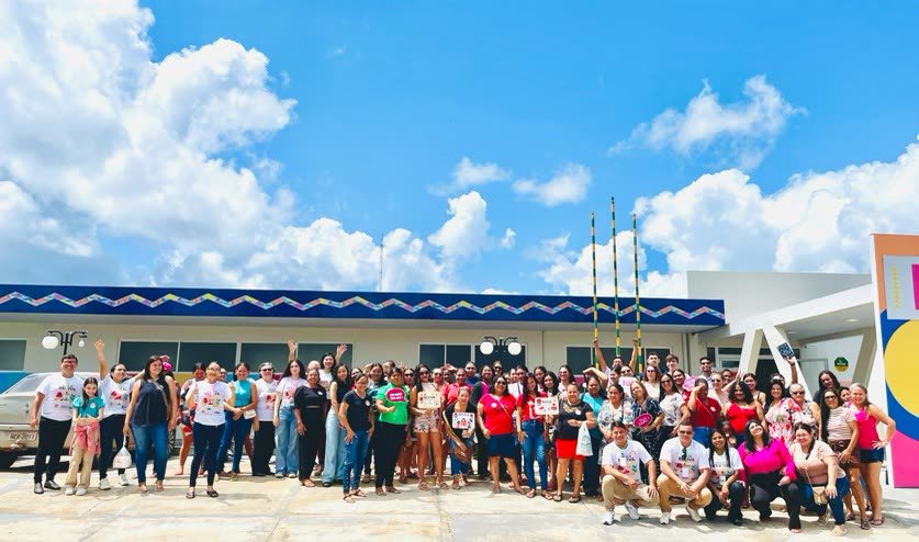 Grande grupo de mulheres reunidas para foto em frente a um prédio, sob céu azul