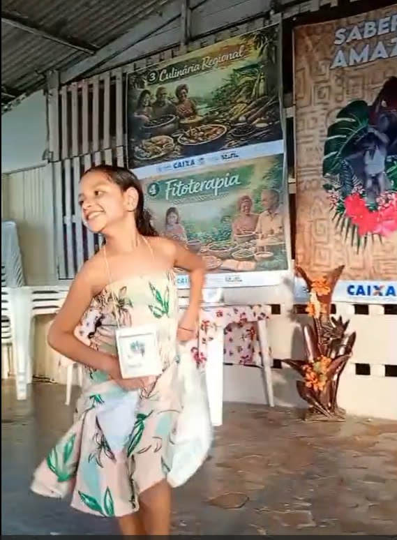 Menina dança carimbó em frente a cartazes sobre culinária regional e fitoterapia